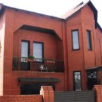 The façade of a two-storey red brick house with the characteristic features of a modern style, but a clear individual character