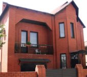 The façade of a two-storey red brick house with the characteristic features of a modern style, but a clear individual character